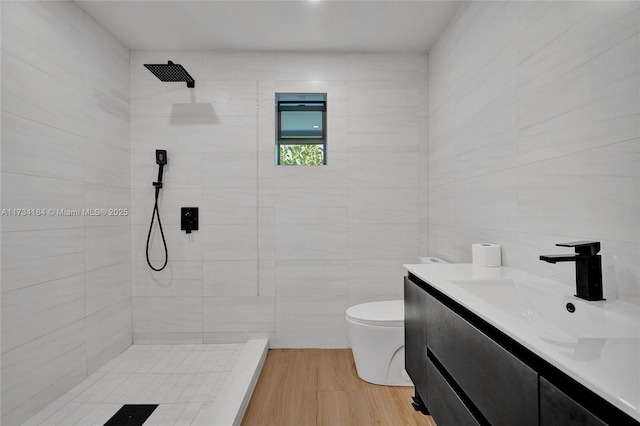 bathroom with toilet, wood-type flooring, tile walls, a tile shower, and vanity