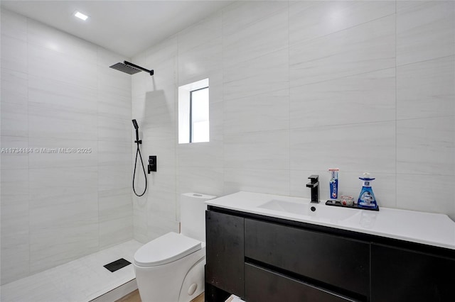 bathroom with tiled shower, vanity, toilet, and tile walls