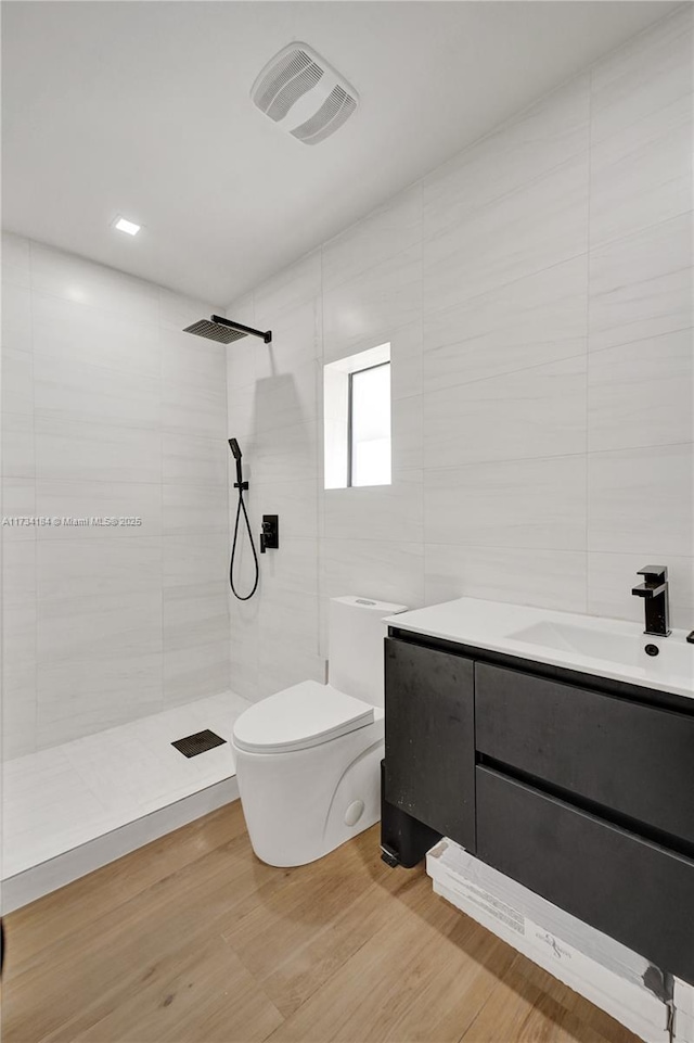 bathroom with hardwood / wood-style floors, tile walls, vanity, tiled shower, and toilet