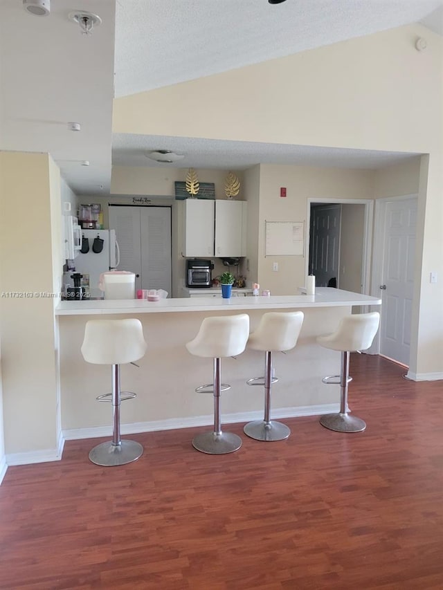 kitchen with a breakfast bar area, white cabinetry, a textured ceiling, dark hardwood / wood-style floors, and kitchen peninsula