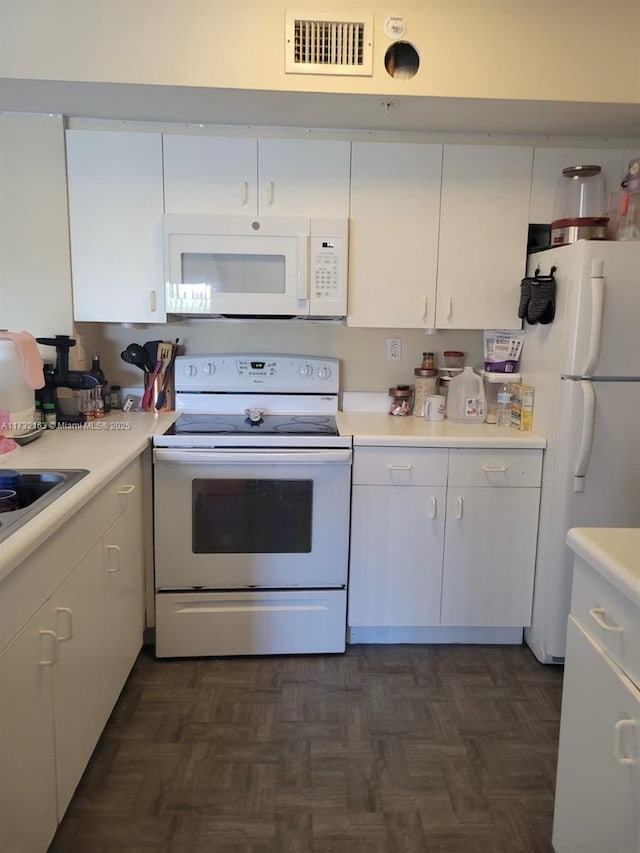 kitchen with sink, white appliances, dark parquet flooring, and white cabinets