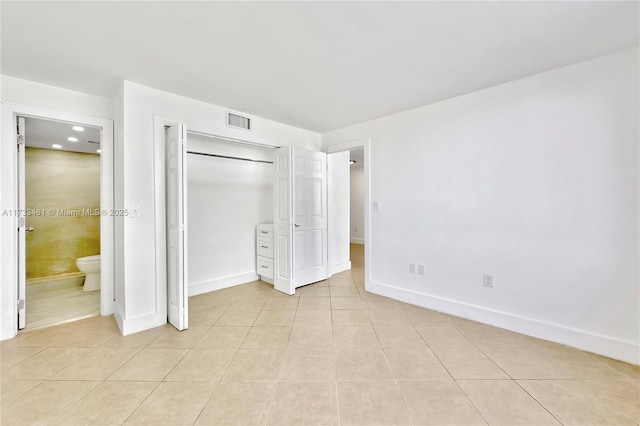 unfurnished bedroom featuring light tile patterned flooring, ensuite bath, and a closet