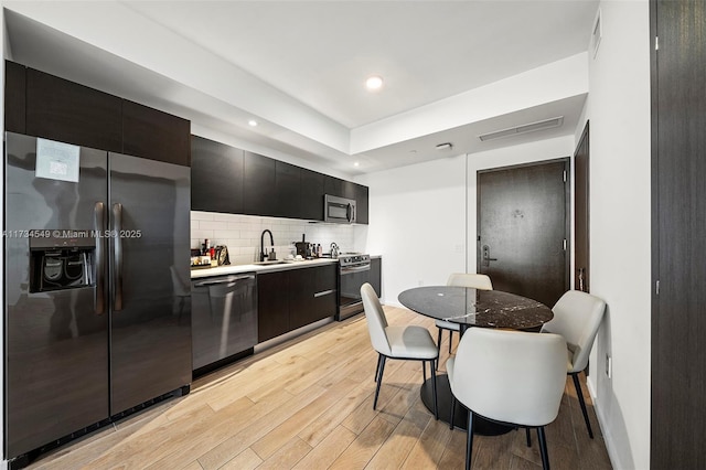 kitchen with light wood finished floors, light countertops, decorative backsplash, appliances with stainless steel finishes, and modern cabinets