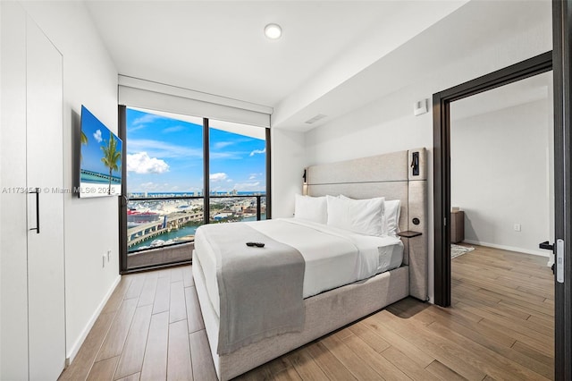 bedroom with expansive windows, light wood-style flooring, and baseboards