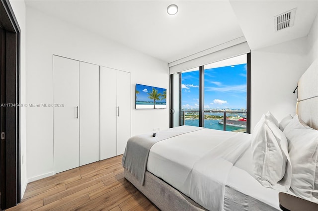 bedroom featuring light wood-style flooring, a water view, visible vents, a closet, and a wall of windows