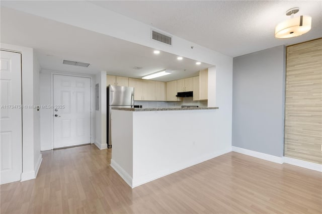 kitchen featuring stainless steel fridge, light hardwood / wood-style floors, kitchen peninsula, cream cabinets, and a textured ceiling