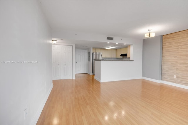 unfurnished living room featuring light wood-type flooring, visible vents, and baseboards