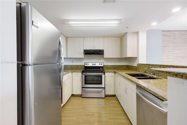 kitchen with sink, stainless steel appliances, light hardwood / wood-style floors, and light stone countertops