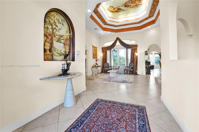 hallway featuring crown molding, a raised ceiling, a high ceiling, and light tile patterned floors