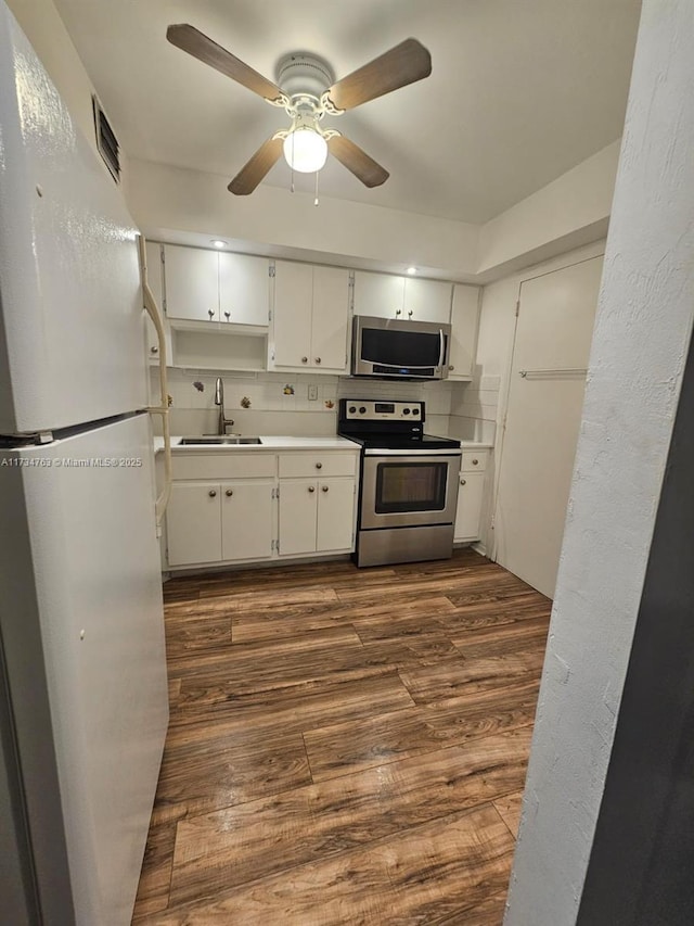 kitchen with appliances with stainless steel finishes, sink, white cabinets, ceiling fan, and dark wood-type flooring