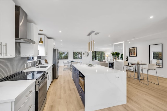 kitchen featuring stainless steel appliances, wall chimney range hood, pendant lighting, and white cabinets