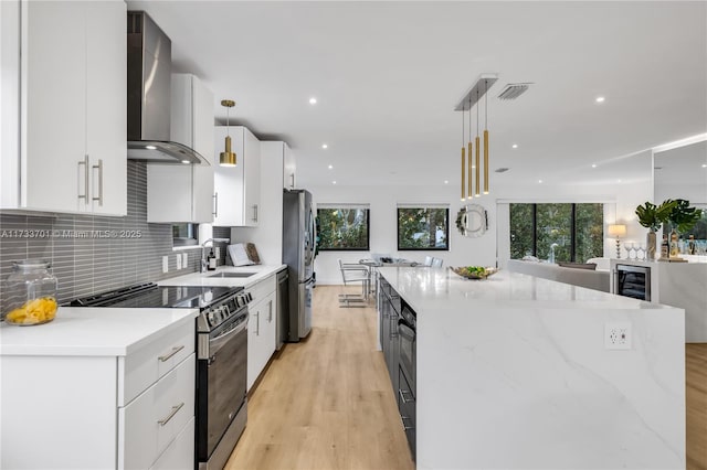 kitchen with pendant lighting, white cabinetry, decorative backsplash, stainless steel appliances, and wall chimney range hood