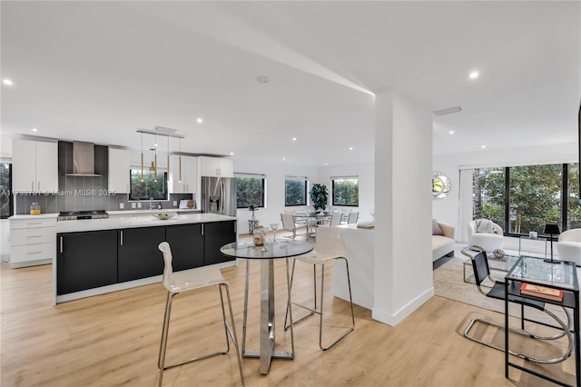 kitchen with pendant lighting, white cabinets, backsplash, a center island, and wall chimney range hood