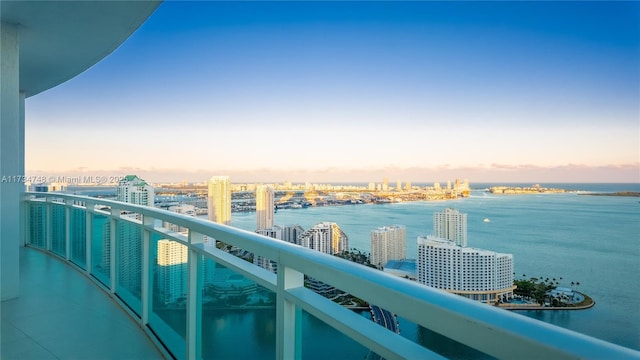 balcony at dusk featuring a water view