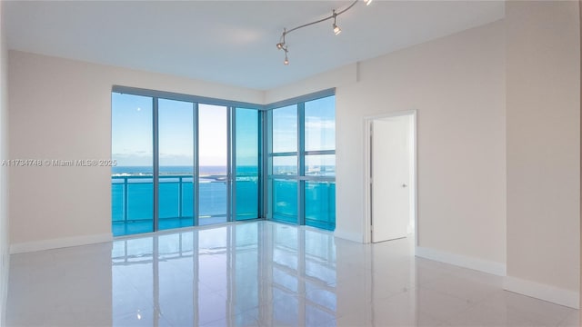 empty room with light tile patterned floors, rail lighting, and a water view