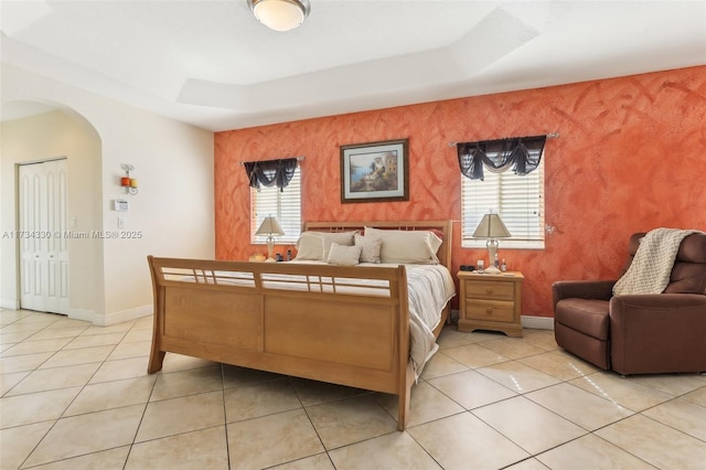 tiled bedroom featuring multiple windows and a tray ceiling