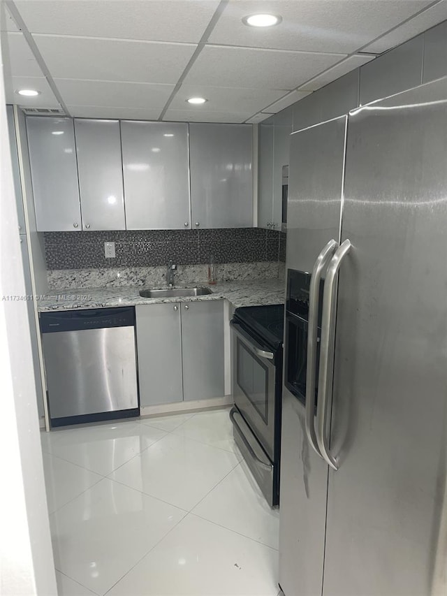 kitchen featuring gray cabinets, appliances with stainless steel finishes, a paneled ceiling, sink, and light stone counters