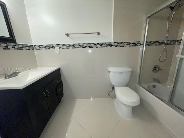 full bathroom with bath / shower combo with glass door, tile walls, tile patterned flooring, vanity, and toilet