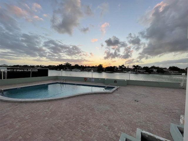 pool at dusk with a patio area and a water view