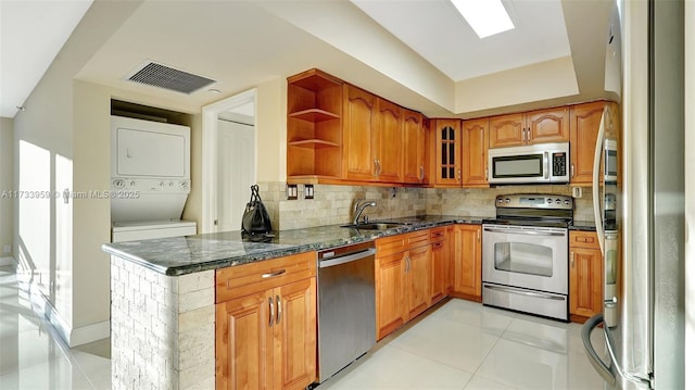 kitchen with stacked washer / drying machine, sink, dark stone countertops, light tile patterned floors, and stainless steel appliances