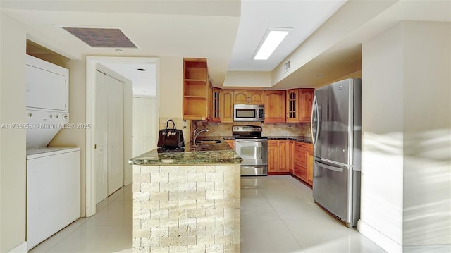 kitchen with stainless steel appliances, stacked washer / dryer, sink, and light tile patterned floors