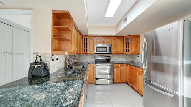 kitchen with appliances with stainless steel finishes, sink, dark stone counters, and light tile patterned floors