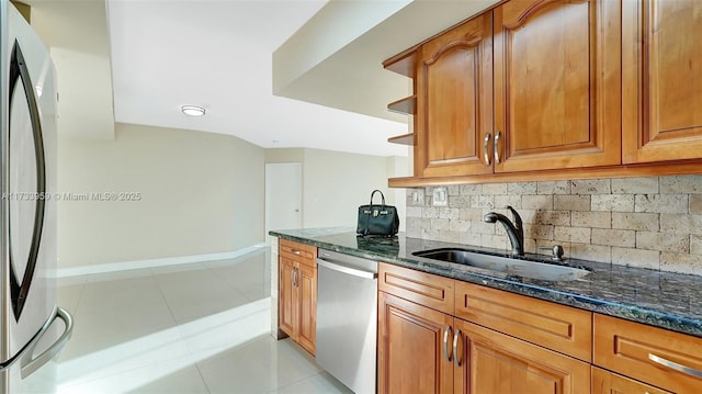 kitchen with sink, light tile patterned floors, dark stone countertops, stainless steel appliances, and decorative backsplash