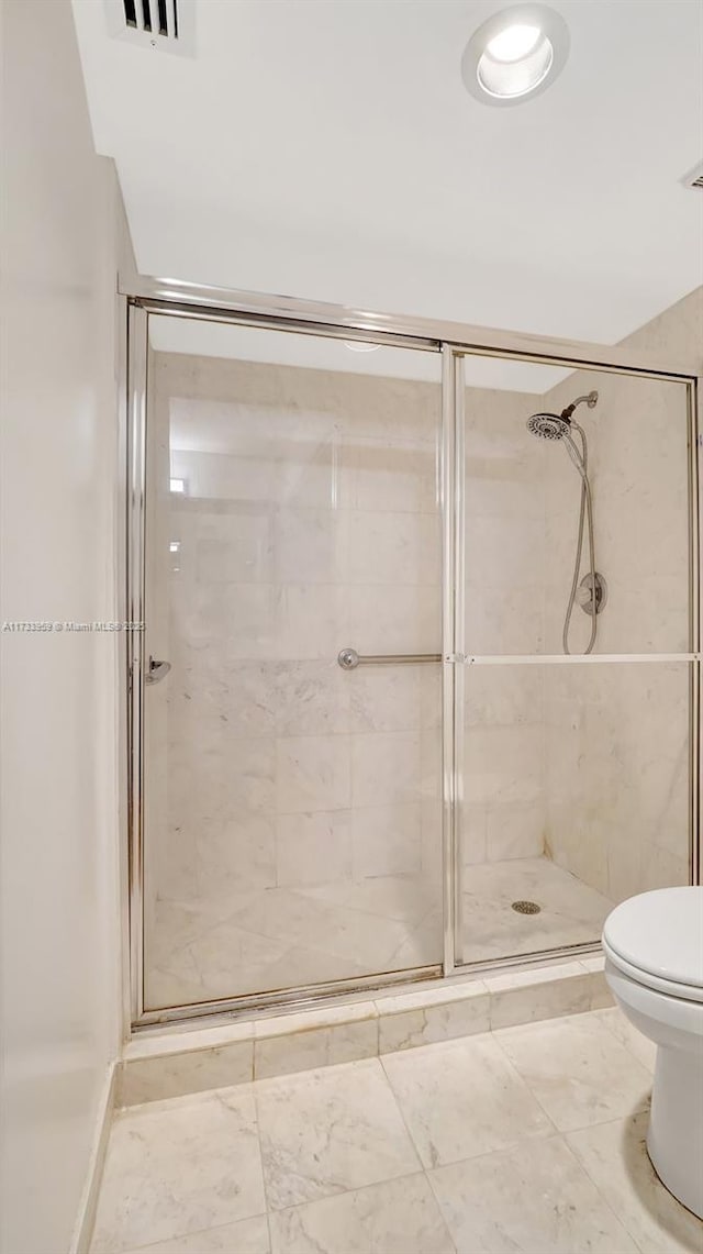 bathroom featuring a shower with door and toilet