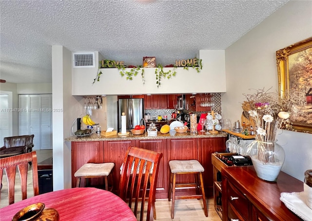 bar featuring stainless steel appliances, backsplash, a textured ceiling, and light hardwood / wood-style flooring