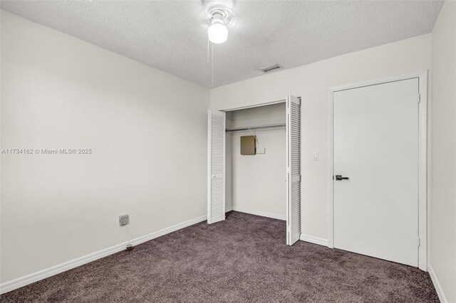 unfurnished bedroom with dark carpet, a closet, and a textured ceiling