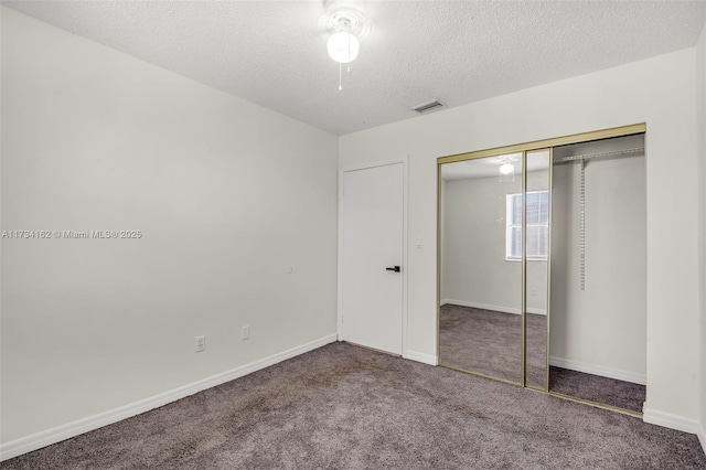 unfurnished bedroom with a closet, a textured ceiling, and dark colored carpet