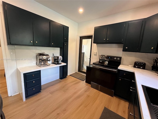 kitchen featuring black electric range oven, light wood-style flooring, dark cabinetry, and light countertops