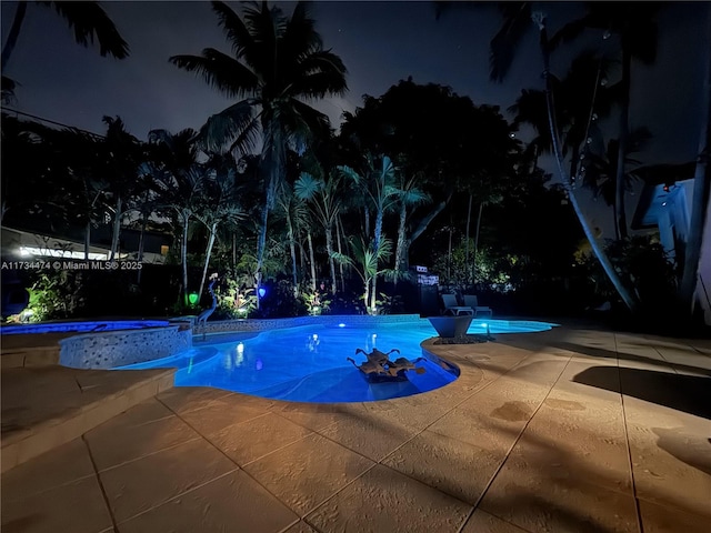 pool at night featuring a patio area