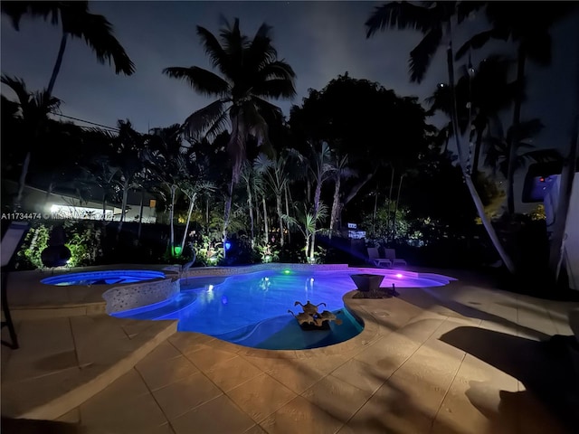 pool at night with a patio area and an in ground hot tub