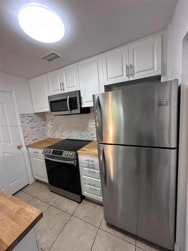 kitchen featuring white cabinetry, butcher block countertops, light tile patterned floors, and stainless steel appliances