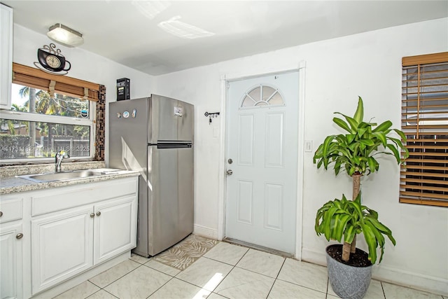 kitchen featuring white cabinets, sink, light tile patterned floors, and stainless steel fridge