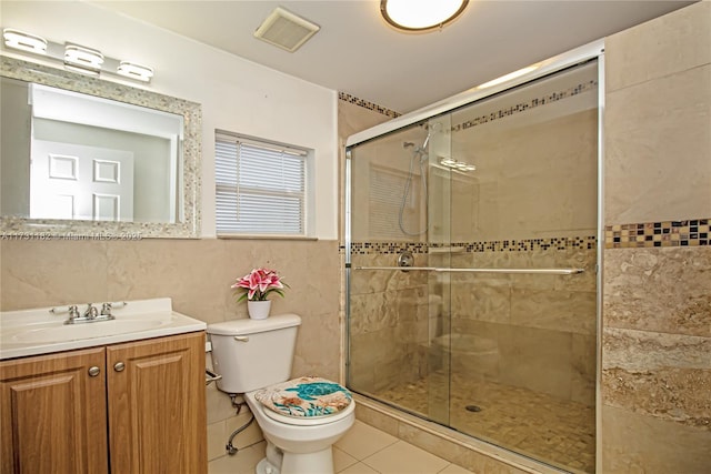 bathroom with a shower with door, tile walls, vanity, tile patterned floors, and toilet