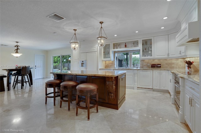 kitchen featuring pendant lighting, a center island, light stone countertops, and white cabinets