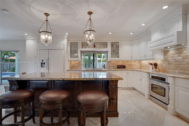 kitchen featuring white cabinets, decorative light fixtures, stainless steel oven, and a kitchen island