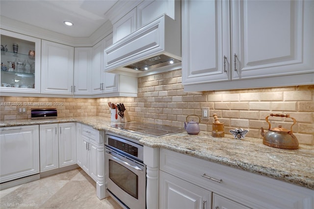 kitchen featuring premium range hood, stainless steel oven, white cabinets, and decorative backsplash