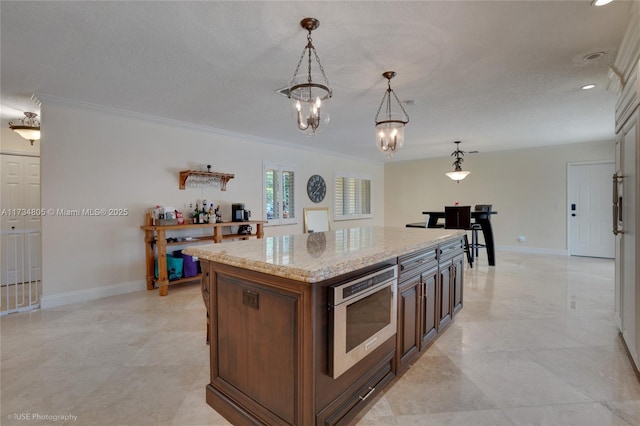 kitchen featuring crown molding, light stone counters, decorative light fixtures, a kitchen island, and wall oven