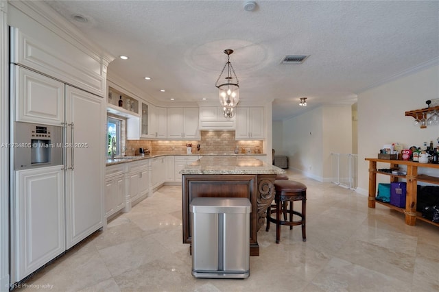 kitchen featuring white cabinetry, tasteful backsplash, decorative light fixtures, a kitchen island, and light stone countertops