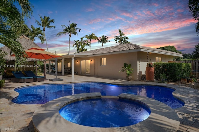 pool at dusk featuring a patio and an in ground hot tub