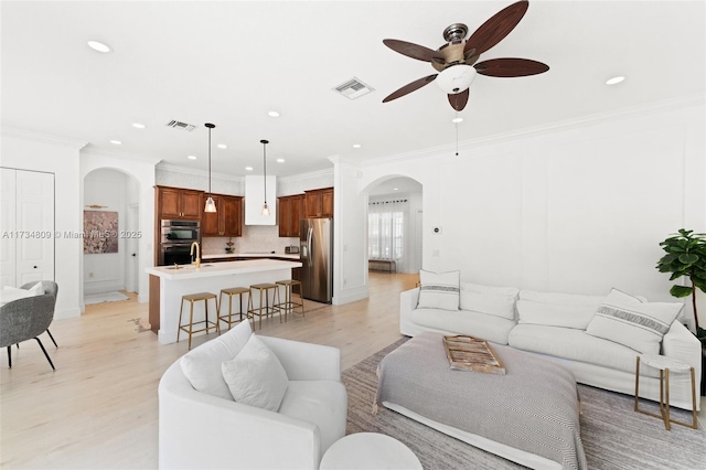 living room featuring light wood finished floors, visible vents, arched walkways, and crown molding