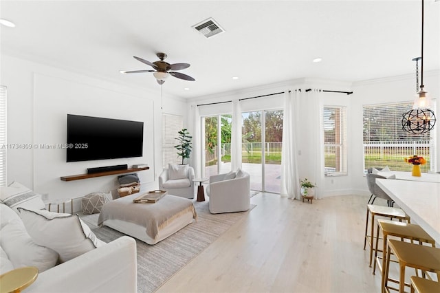 living area featuring light wood-style flooring, recessed lighting, ceiling fan with notable chandelier, visible vents, and crown molding