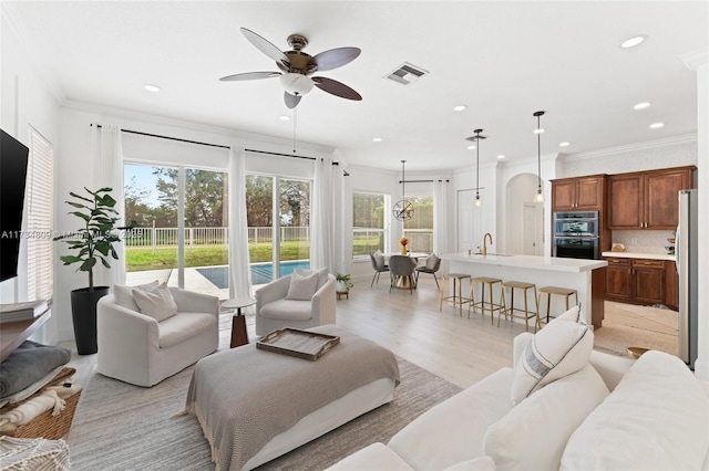 living room with light wood finished floors, visible vents, arched walkways, and ornamental molding