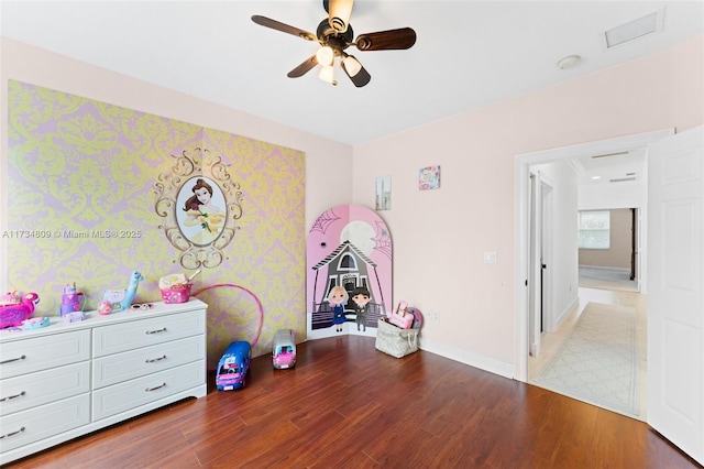 recreation room featuring a ceiling fan, visible vents, baseboards, and wood finished floors