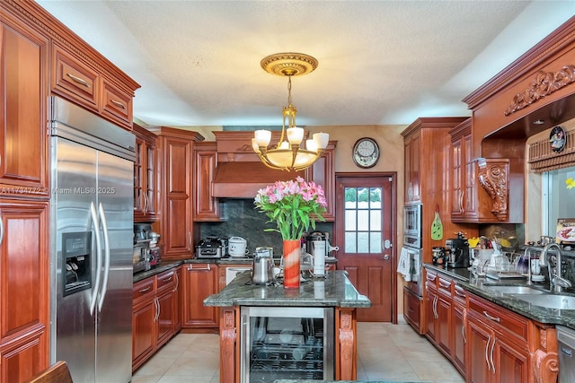 kitchen featuring beverage cooler, built in appliances, sink, and dark stone counters