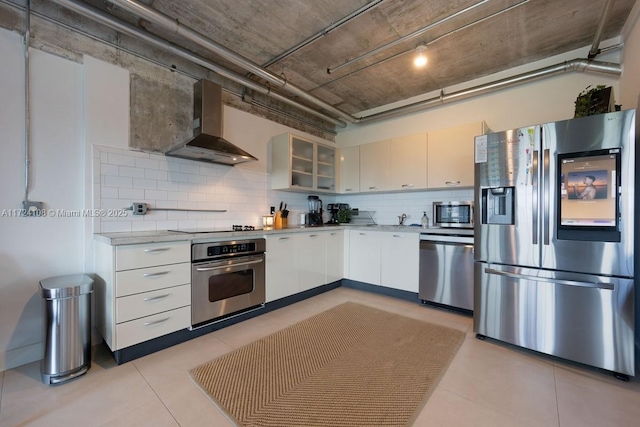 kitchen featuring white cabinetry, light tile patterned floors, appliances with stainless steel finishes, wall chimney range hood, and backsplash