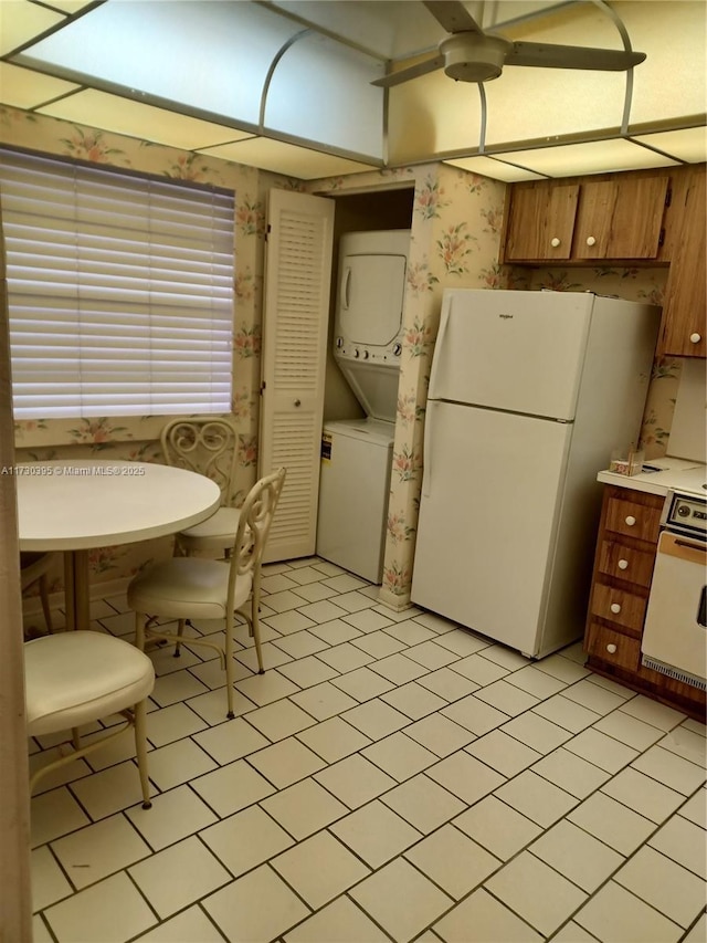 kitchen featuring light tile patterned flooring, oven, stacked washer and clothes dryer, and white refrigerator